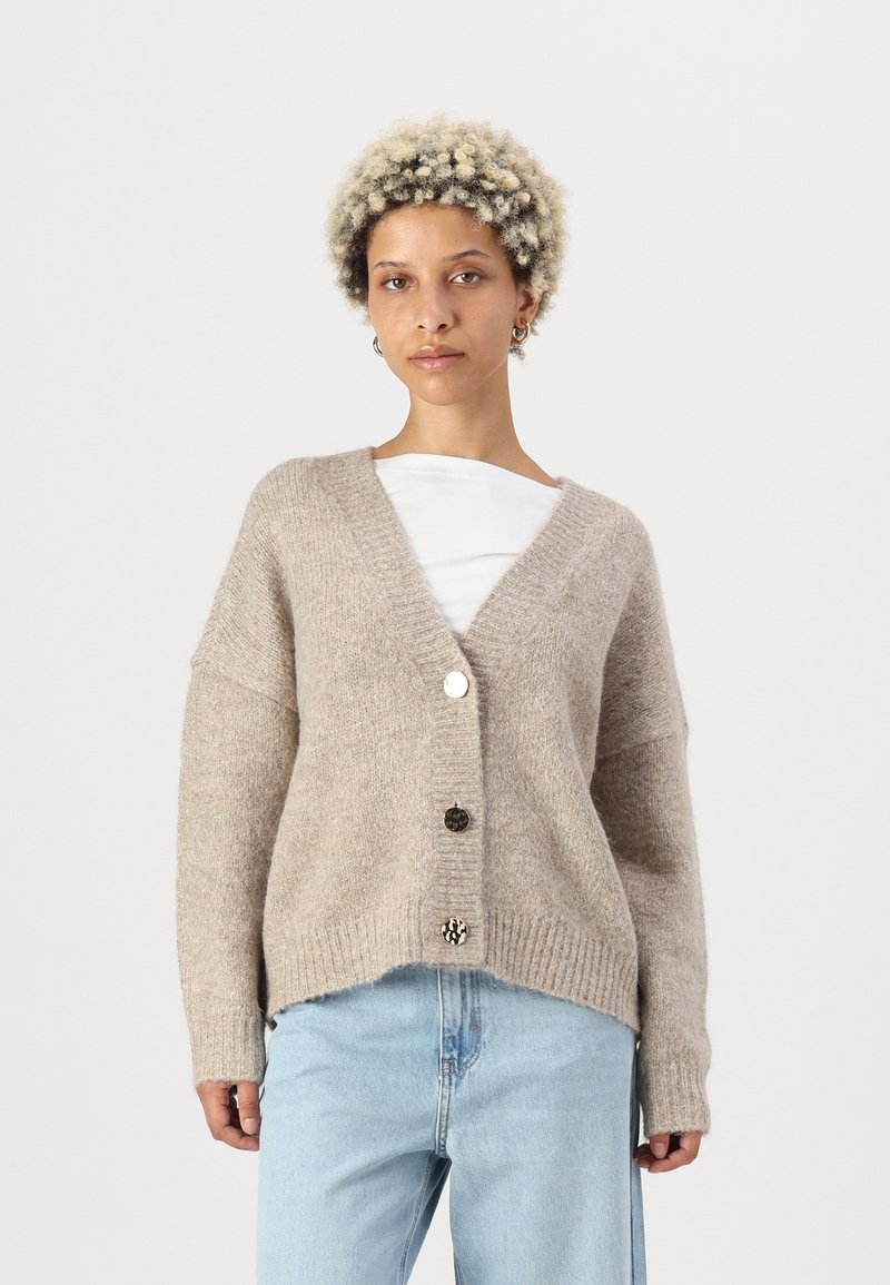 Beige gestrickte Cardigan mit langen Ärmeln, V-Ausschnitt, strukturiertem Stoff und fünf Knopfverschluss mit einer Mischung aus runden und gemusterten Knöpfen.