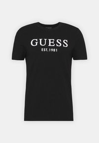 Sort bomulds t-shirt med hvid tekst "GUESS EST.1981" på forsiden. Korte ærmer og rund halsudskæring. Glat tekstur.