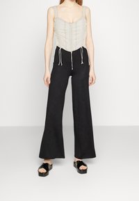 Ljusbeige korsettopp med rynkade detaljer och justerbara band, tillsammans med svarta vida byxor och blanka svarta platåsandaler.