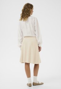 Kreemivärvi kudumiga seelik, millel on laienev äär, kombineeritud valge pikkade varrukatega pluusiga. Mudel kannab beeži baleriini sussikesi ja valgeid pahkluusokke.