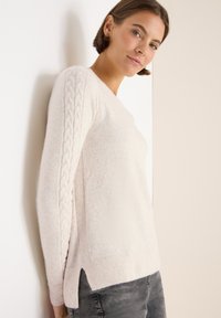 Helles rosa Sweatshirt mit Kabelstrickdetails an den Ärmeln, geripptem Saum und seitlichen Schlitzen; weiche Textur, runder Ausschnitt und entspannte Passform.