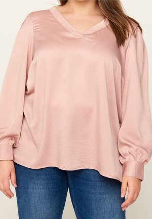 Jasnoróżowa, satynowa bluzka z dekoltem w szpic i długimi bufkowatymi rękawami. Charakteryzuje się luźnym krojem i elastycznymi mankietami. W zestawieniu z niebieskimi dżinsami.