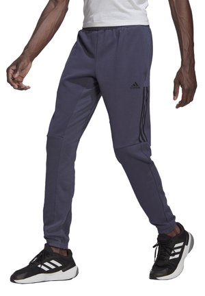 Pantalones deportivos azul marino de corte entallado, con cintura elástica, bolsillos laterales y detalles de rayas negras. Combinados con zapatillas deportivas negras.