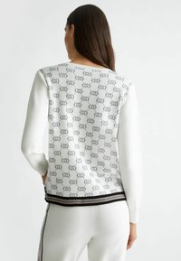 Maglione bianco a fantasia con un design del logo grigio, maniche lunghe, polsini a coste e una striscia a contrasto nera e dorata sull'orlo.