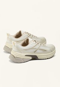 Sportliche Sneakers aus cremigem Mesh mit beigen Akzenten. Sie verfügen über eine klobige Sohle, strukturierte Overlays und eine Schnürung für einen sicheren Halt.