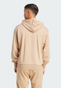 Sudadera beige con un bolsillo tipo canguro, corte relajado y capucha ajustable con cordones. Textura suave y puños y dobladillo acanalados.