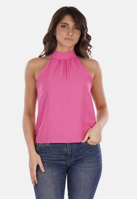 Top rosa con scollo a halter, caratterizzato da un collo arricciato e un tessuto morbido e testurizzato. Abbinato a jeans blu scuro, che evidenziano un fit rilassato.