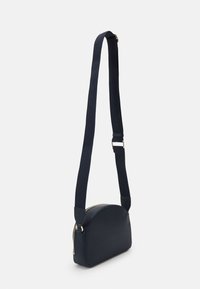 Borsa a tracolla in pelle blu navy con fondo arrotondato, zip dorata e tracolla testurizzata blu navy. Presenta un design minimalista.