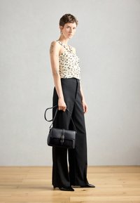 Geantă de piele neagră cu clapetă frontală și detaliu cu cataramă, asortată cu un top bej cu model și fără mâneci și pantaloni negri lejeri.