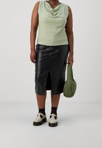 Jasnozielona, teksturowana bluzka bez rękawów, czarna skórzana spódnica midi z rozcięciem z przodu, zielona torebka pikowana i kremowe buty z czarną podeszwą.