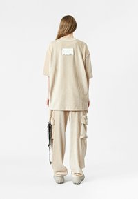 Camiseta oversize de pana beige con mangas cortas, que presenta una etiqueta de logo en la parte posterior. Combinada con pantalones cargo a juego y zapatillas grises gruesas.