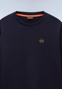 T-shirt en coton bleu marine avec un col rond, bord intérieur orange et un petit logo circulaire comportant des accents noirs, blancs et orange.