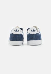 Navy suede sneakers with white accents, featuring a textured rubber sole and a logo patch on the heel. Simple and classic design.