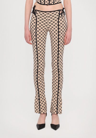 Pantaloni beige con un motivo a monogramma nero, caratterizzati da piping laterale nero, orli a zampa e un design aderente.