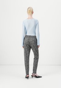Lyseblå ribbet langermet topp, grå bukser med svart leopardmønster, og svarte hælsandaler. Enkelt design, kroppsnær silhuett.