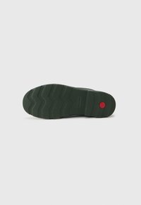 Semelle en caoutchouc vert avec un motif de bande de roulement en zigzag et un accent circulaire rouge, conçu pour l'adhérence et la durabilité. Profil plat avec une surface texturée.