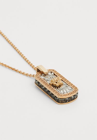 Halskette in Goldfarbe mit einem rechteckigen Anhänger, der mit einem reliefartigen Löwenkopf verziert ist, geschmückt mit klaren und dunklen Glassteinen.