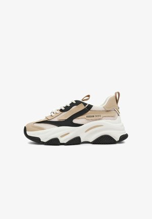 Sneaker chunky beige e nero con suola spessa bianca, dettagli in mesh e pelle, e asola sul tallone, marchio Steve Madden sul lato.