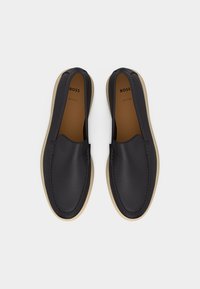 Paar schwarze Leder-Slipper mit beigen Sohlen und der Marke "BOSS", von oben auf weißem Hintergrund gezeigt.