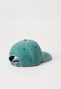 Boné de basebol em algodão na cor verde-teal desbotado, com visor curvo, faixa ajustável e costuras em contraste nas emendas.