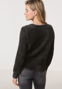 Dunkelgrauer, flauschiger Strickpullover mit rundem Ausschnitt. Lange Ärmel und ein leicht verkürzter Saum. Kombiniert mit dunklen Jeans.