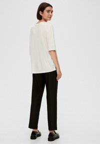 Luźna, kremowa koszulka z okrągłym dekoltem, zestawiona z czarnymi spodniami w prostym kroju i czarnymi butami wsuwanymi. Prosty i minimalistyczny design.