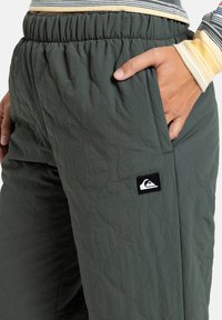 Gequiltte groene broek met een elastische tailleband en zijzakken. Heeft een klein zwart merkembleem op de bovenkant van de dij.