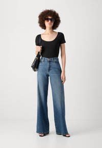 Svart kortärmad topp i kombination med högmidjade, vida blå jeans. Tillbehören inkluderar stora mörka solglasögon och en liten svart handväska.