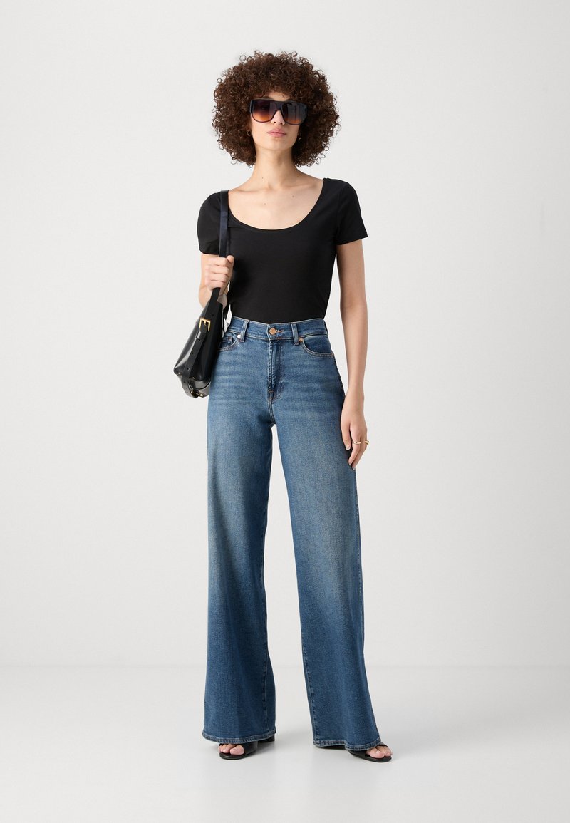 Haut noir à manches courtes associé à un jean bleu à taille haute et jambes larges. Les accessoires comprennent de grandes lunettes de soleil noires et un petit sac à main noir.