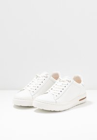 Sneakers in pelle bianca con texture liscia, punta arrotondata e design a profilo basso. Presentano un sottile accento in tan e una suola decorata.