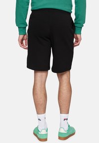 Pantalones cortos de algodón negros con bolsillos laterales, con una textura suave y una cintura elástica. Llevados con zapatillas verdes y calcetines blancos.