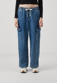 Pantalones cargo de mezclilla en azul claro con cinturilla elástica y cordón, que cuentan con bolsillos laterales y un diseño holgado de pierna ancha.
