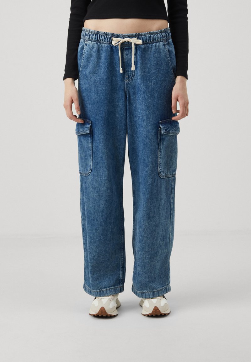 Pantalones cargo de mezclilla en azul claro con cinturilla elástica y cordón, que cuentan con bolsillos laterales y un diseño holgado de pierna ancha.