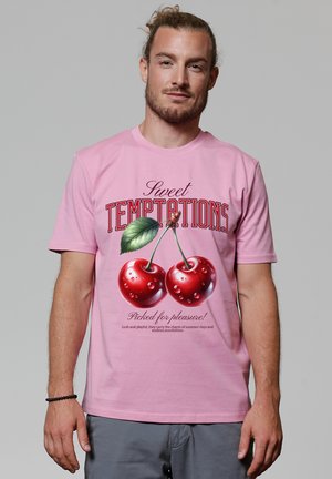 Roze katoenen T-shirt met een kleurrijke afbeelding van kersen met druppels, en tekst erboven die "Sweet Temptations" zegt en eronder "Picked for pleasure!".