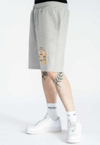 Shorts grigi con elastico in vita e tasche laterali. Presentano un design ricamato giallo. Sneakers bianche e calzini a fantasia completano il look.