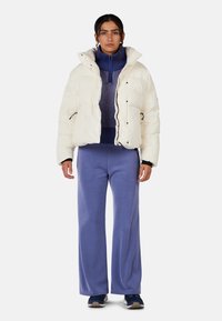 Giacca puffa bianca con design a trapunte, indossata sopra un dolcevita blu scuro. Abbinata a pantaloni larghi blu chiaro e sneakers blu navy.