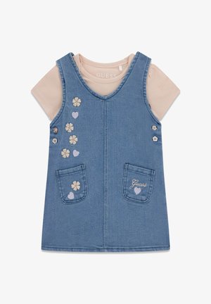 Robe salopette en denim bleu avec des fleurs et des cœurs brodés, poches avant, et chemise beige à manches courtes en dessous.
