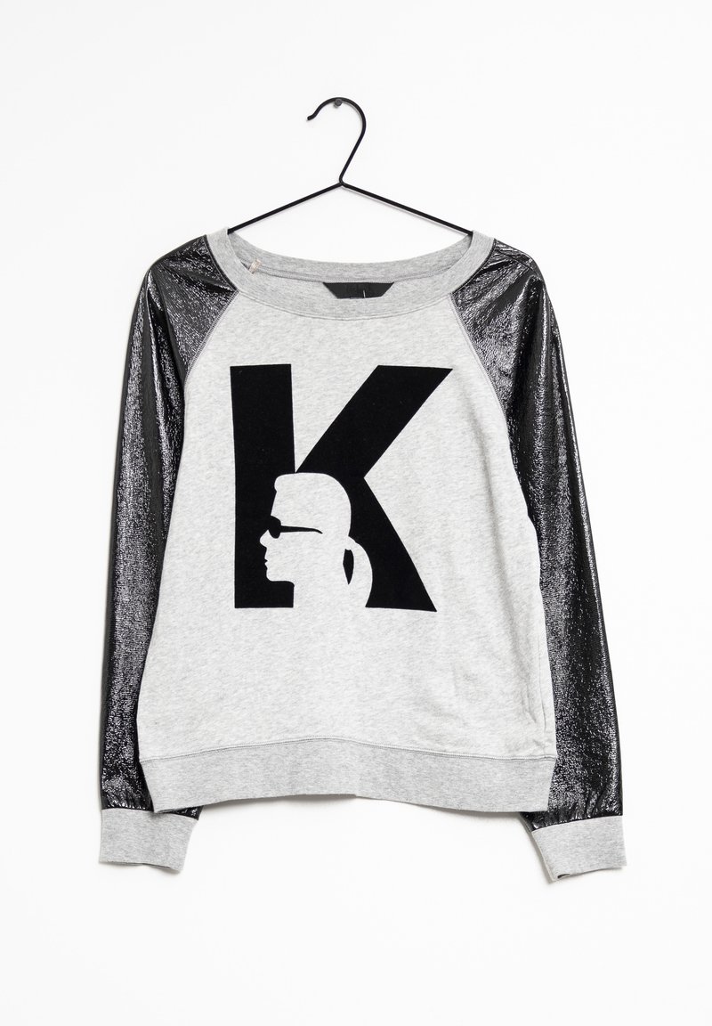 Sweat-shirt gris avec manches longues noires brillantes, grande lettre noire "K" sur le devant, silhouette d'une personne portant des lunettes de soleil à l'intérieur de la lettre.