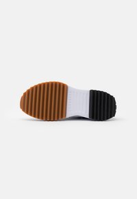 Semelle de chaussure en caoutchouc avec des sections orange, blanche et noire. Stries texturées et logo détaillé sur la section blanche pour une meilleure adhérence.
