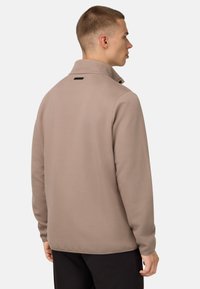 Pullover beige strutturato con colletto alto, dotato di un'etichetta nera di accento sul retro e maniche lunghe. Tessuto morbido e vestibilità comoda.