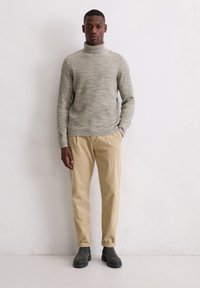 Gestrickter grauer Rollkragenpullover kombiniert mit beigen Cordhosen und grauen Stiefeletten. Das Outfit zeichnet sich durch eine lockere Passform und strukturierte Stoffe aus.