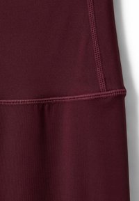 Bordo sportinė medžiaga su lygiu paviršiumi, turinti plokščias siūles ir prigludusį dizainą, tinkama aktyviam naudojimui.