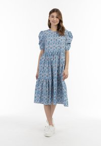 Rochie florală albastră cu mâneci bufante, talie strânsă și fustă în straturi. Materialul are mici flori roz și albe pe un fundal de un albastru deschis.