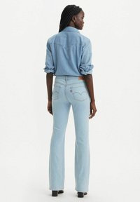 Pantalones de mezclilla claros de campana con cintura alta, bolsillos traseros con detalle del logo, combinados con una camisa de mezclilla clara a juego.
