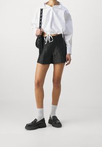 Sorte shorts med snoretræk og sideakcenter. Sættet er kombineret med en hvid cropped t-shirt og sorte platform sko over grå sokker.
