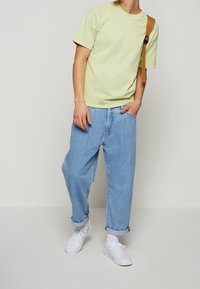 Ljust grön bomull t-shirt med korta ärmar, matchad med lösa blå denimjeans och vita sneakers, samt en brun axelremsväska.