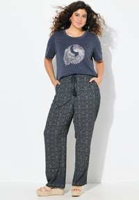 Marineblauw graphic t-shirt met een wit, gestileerd vogelontwerp; gecombineerd met losse, gemusterde broeken in marineblauw en groen met een koord in de taille.