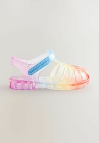 Permatomos basutės turi vaivorykštės spalvų gradientą, spalvotas dirželius ir tekstūruotą pado paviršių. Dizainas apima kelias skylutes, skirtas oro pralaidumui.