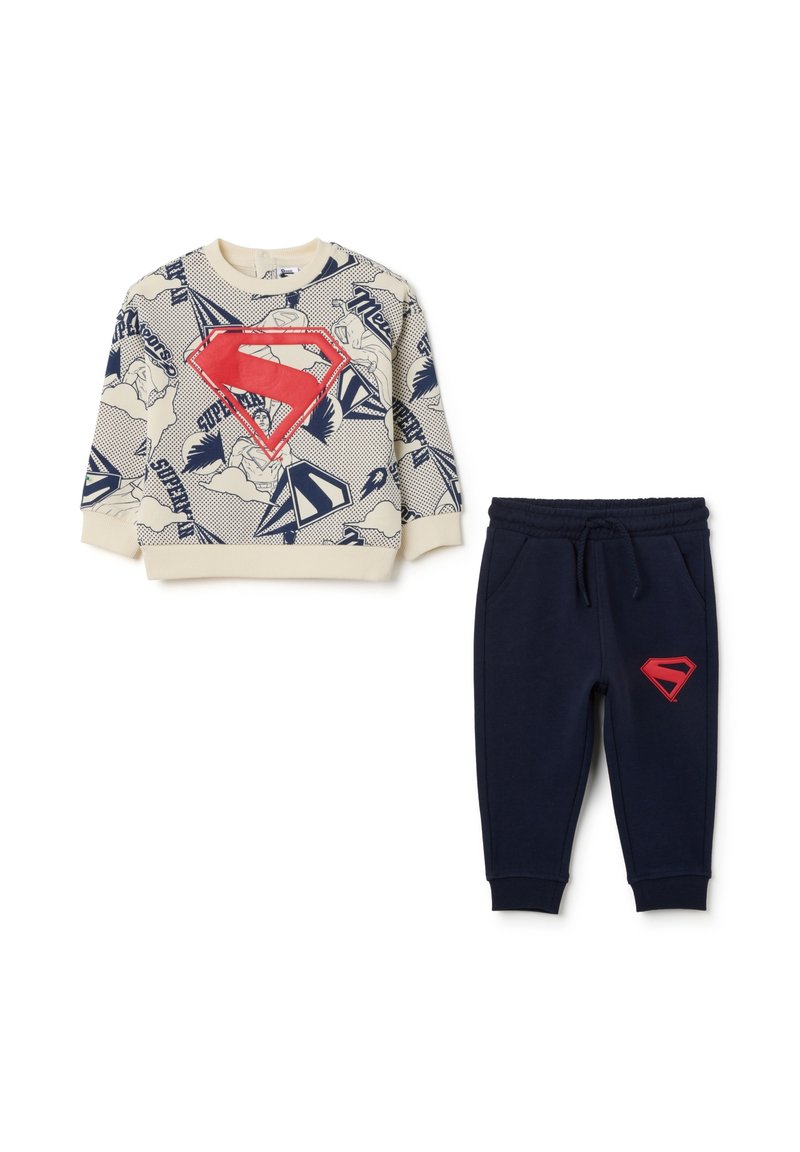 Sudadera con base crema, estampado de cómic azul y un gran logo rojo de Superman; joggers azul marino con logo rojo en la pierna; ambos en tela suave.