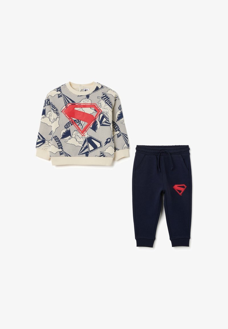 Sudadera con base crema, estampado de cómic azul y un gran logo rojo de Superman; joggers azul marino con logo rojo en la pierna; ambos en tela suave.